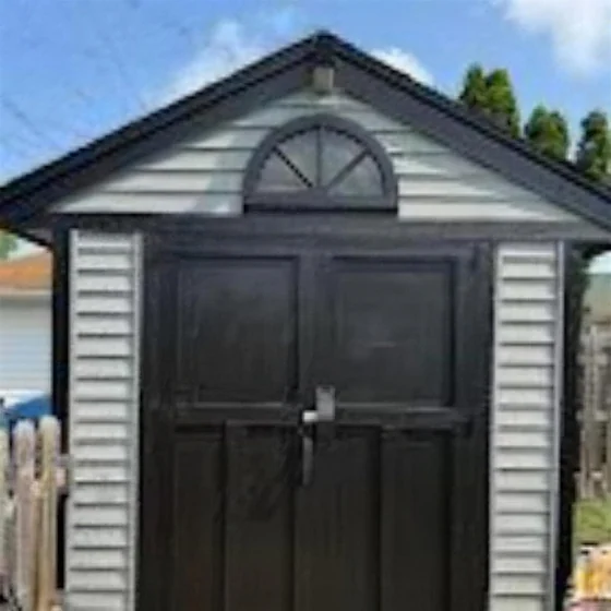 A garage with double doors finished in near black against pale siding, a painted sunburst in the gable above