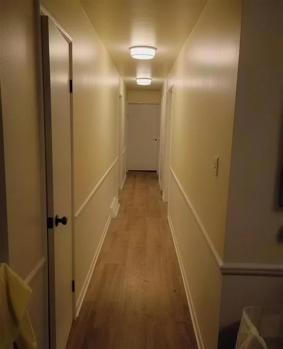 An interior hallway painted in a warm off white with white trim and a wood floor